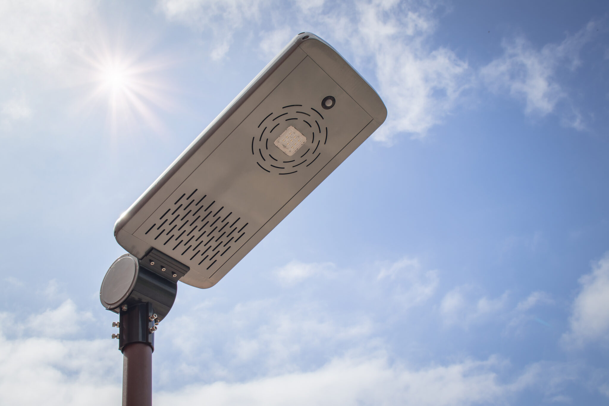 Close up solar street lamp on metal pole with blue sky and sunlight in background.